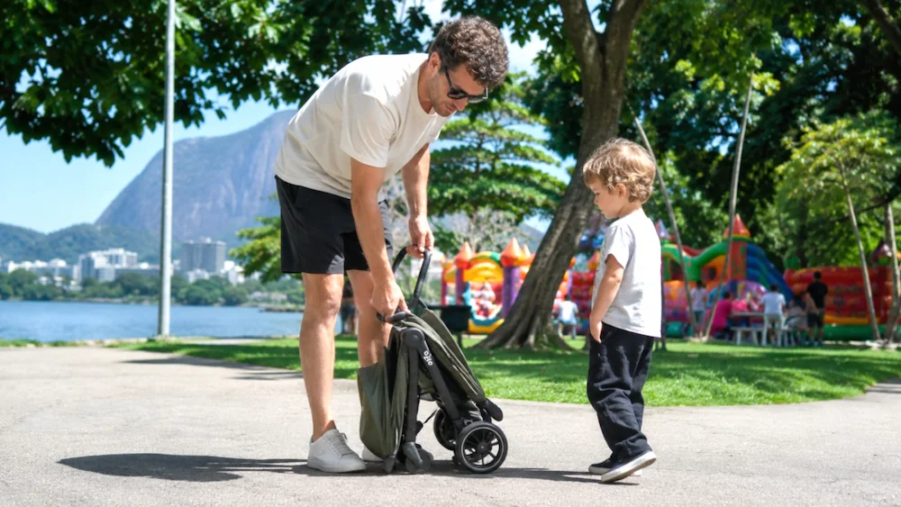 Pai dobrando carrinho de bebê compacto com uma mão no calçadão de Ipanema, Rio de Janeiro